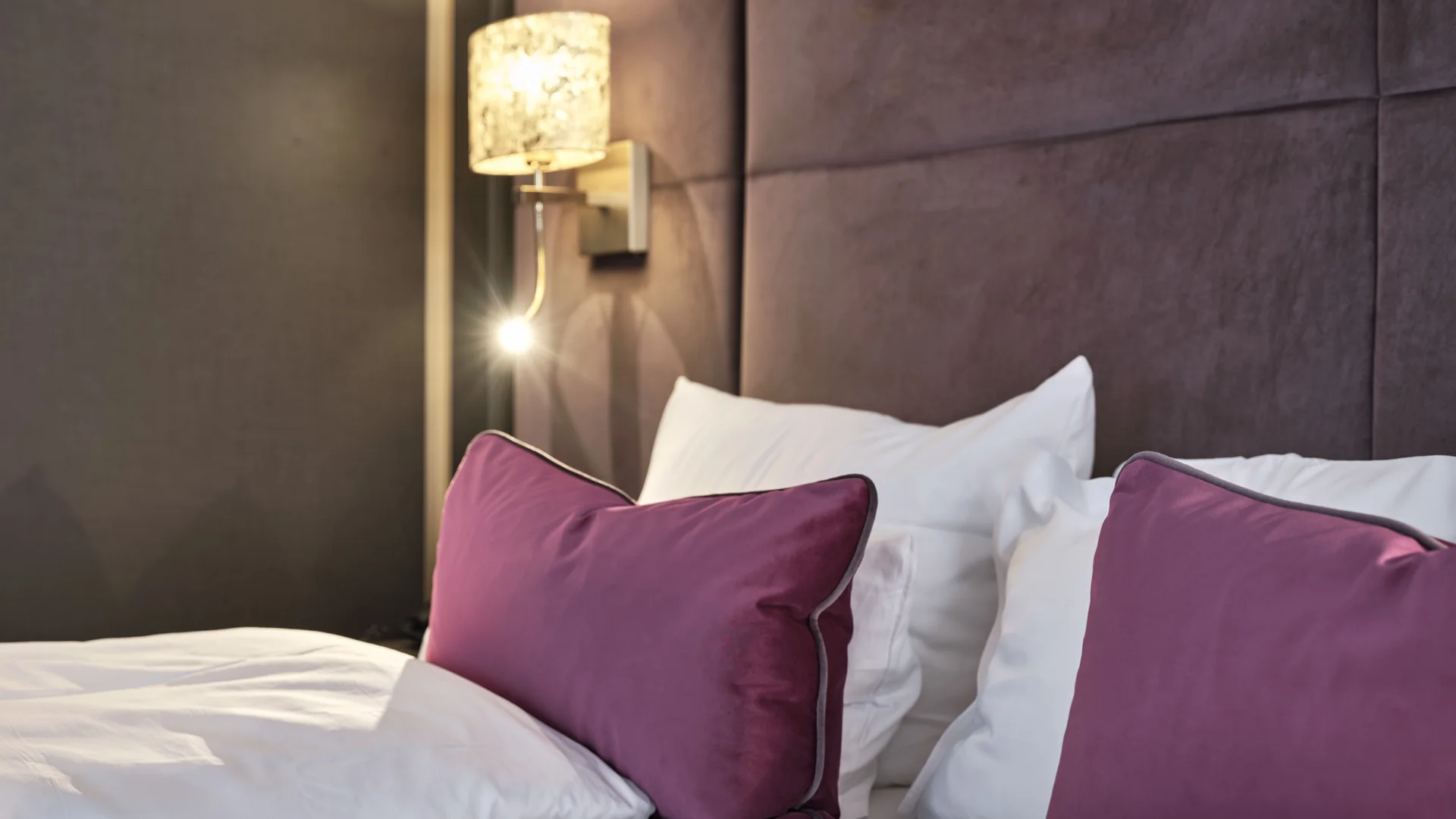 Reppert, Ihr Hotel in Hinterzarten im Schwarzwald Gemütliches Bett mit lila Kissen und sanfter Wandbeleuchtung