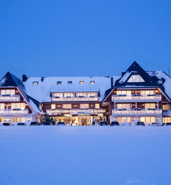 Reppert, Ihr Hotel in Hinterzarten im Schwarzwald Beleuchtetes Hotel im Chaletstil in einer verschneiten Winterlandschaft bei Dämmerung