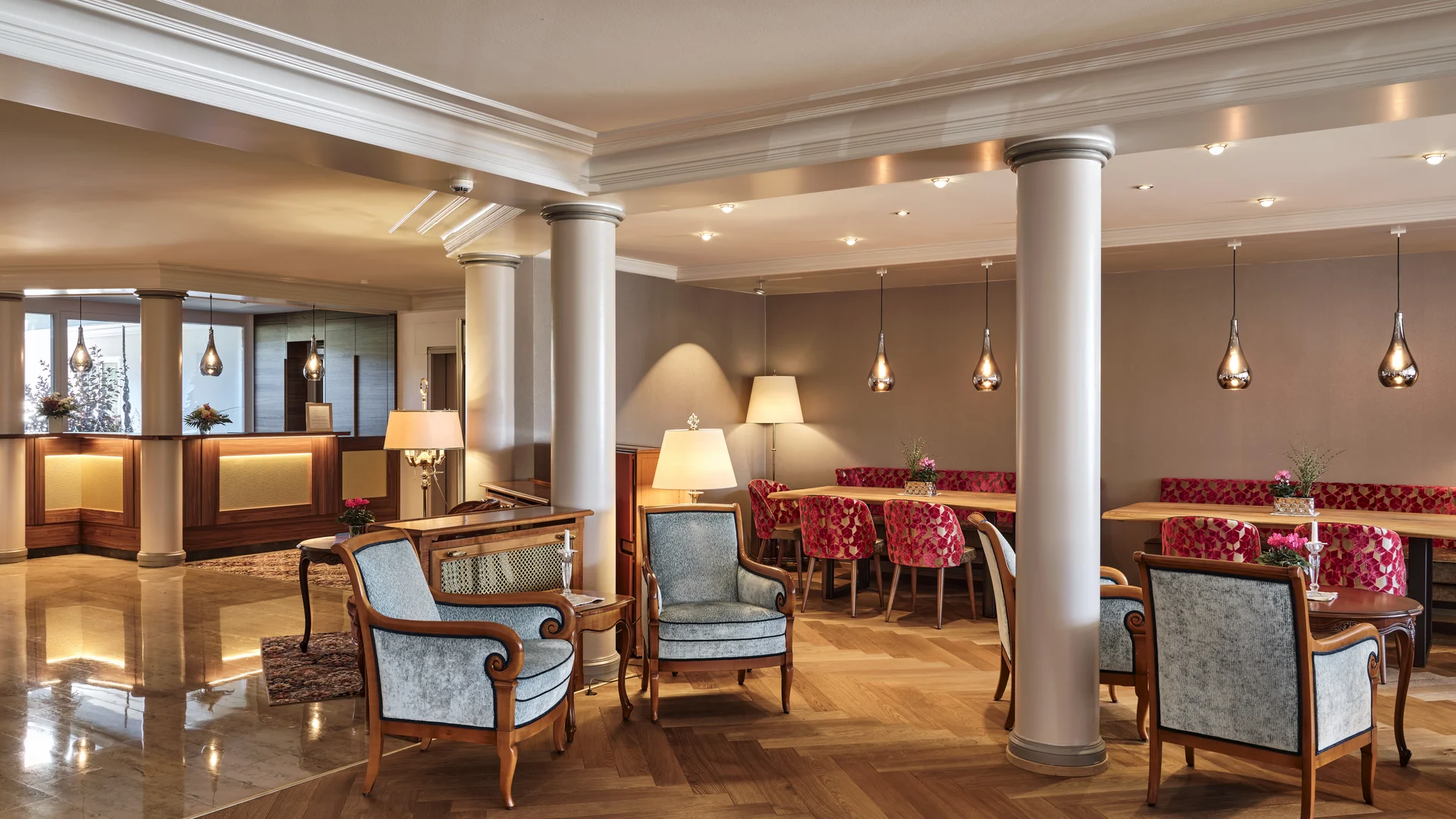 Reppert, Ihr Hotel in Hinterzarten im Schwarzwald Heller Hotel-Lobbybereich mit Säulen, Sesseln und roten gepolsterten Stühlen