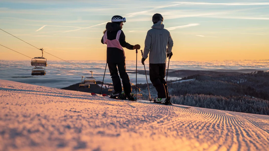 Reppert, Ihr Hotel in Hinterzarten im Schwarzwald Zwei Skifahrer auf einer verschneiten Piste mit Bergblick im Abendlicht