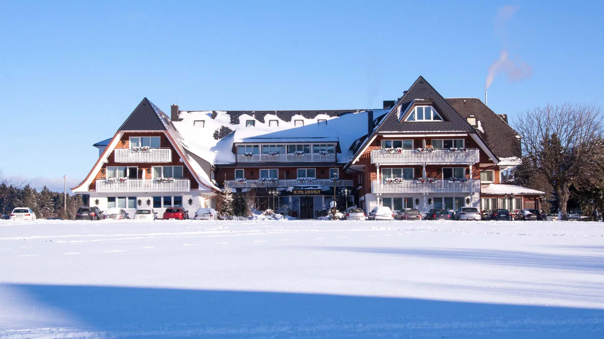 Reppert, Ihr Hotel in Hinterzarten im Schwarzwald Hotel mit verschneitem Dach vor einer weitläufigen Schneelandschaft