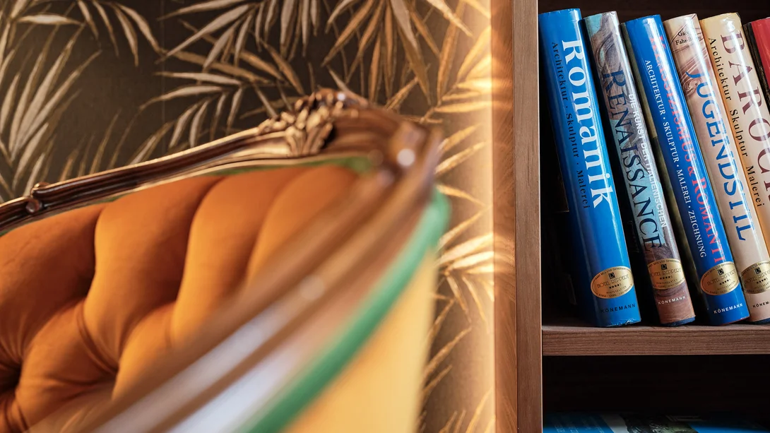 Reppert, Ihr Hotel in Hinterzarten im Schwarzwald Nahaufnahme eines Bücherregals mit Architektur- und Kunstbüchern neben einem orangefarbenen Sessel