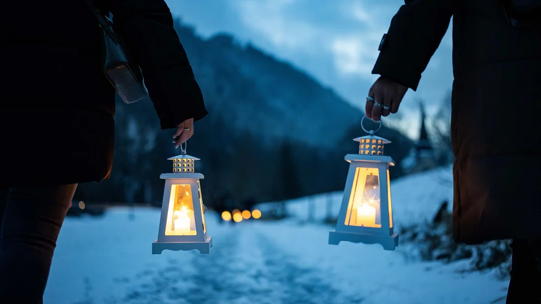 Reppert, Ihr Hotel in Hinterzarten im Schwarzwald Zwei Personen tragen leuchtende Laternen auf einem verschneiten Weg vor Bergkulisse