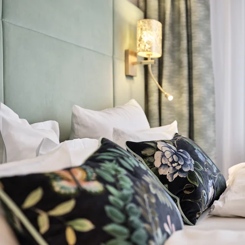 Reppert, Ihr Hotel in Hinterzarten im Schwarzwald Moderne Schlafzimmerwand mit Leuchte und dekorativen floral gemusterten Kissen